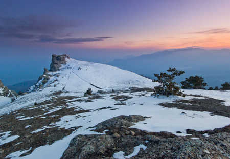 snow-covered mountains and rocks at purple sunset with clouds on skyの写真素材