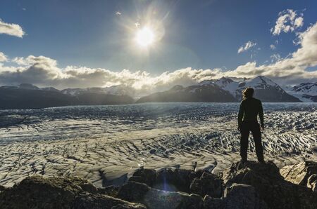 man standing on the stone above Grey glacier in patagonia at sunsetの写真素材