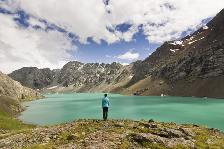 girl in blue jacket standing above blue lake with mountains surroundedの写真素材