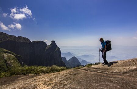 man with backpack standing on top of mountain with blue sky with cloudsの写真素材