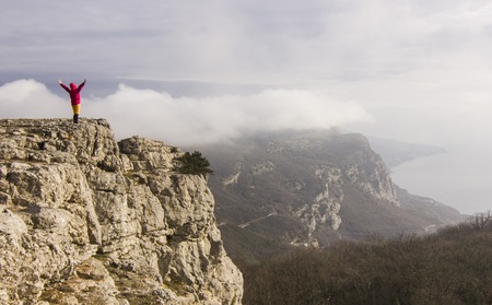 girl with hands up standing on a cliff in mountainsの写真素材