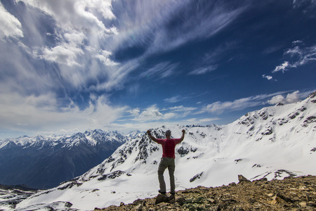 man standing on a cliff in snowy mountains with hands upの写真素材
