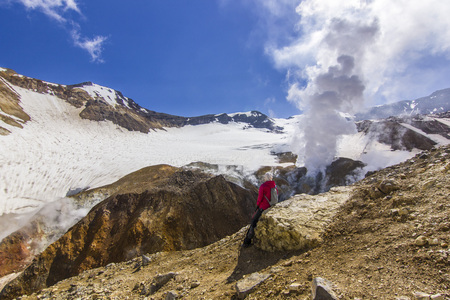 girl sitting near steaming crater of active volcano covered by snow