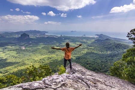 man with hands up standing on rock at sunset with mountains below