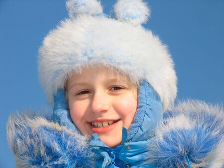 Winter portrait of laughing young girl on blue sky background