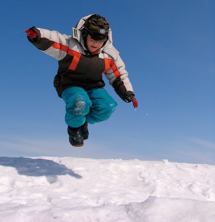 Boy jumping over snow on blue skyの写真素材