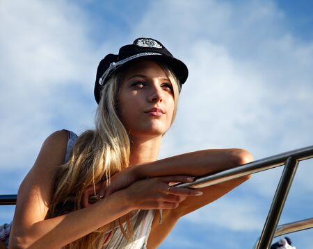 young beautiful blonde in captain's hat outdoors, posing on yachtの写真素材