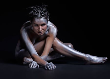 portrait of nude girl body painted with silver sitting on blackの写真素材