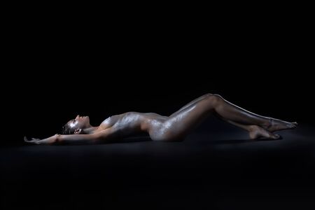portrait of nude girl body painted with silver laying on blackの写真素材