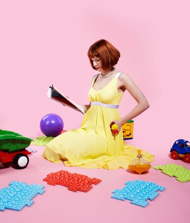 portrait of redhead woman reading magazine with various toys aroundの写真素材