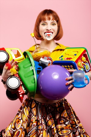 portrait of redhead woman posing with various toys on pinkの写真素材