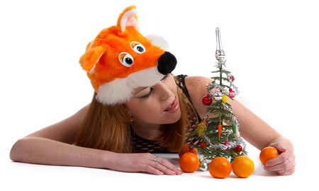 portrait of beautiful redhead pale skinned model in foxface festival hat laying with little new year tree and mandarinesの写真素材