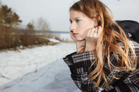 Blonde girl near winter river covered by ice