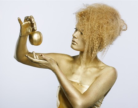 portrait of girl with golden bodyart posing with golden apple in her hands on grayの写真素材
