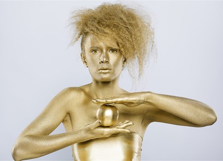 portrait of girl with golden bodyart posing with golden apple in her hands on grayの写真素材