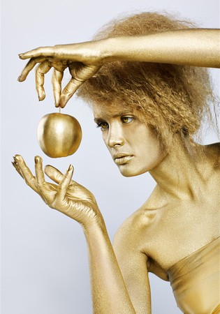 portrait of girl with golden bodyart posing with golden apple in her hands on grayの写真素材