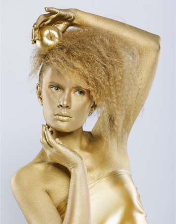 portrait of girl with golden bodyart posing with golden apple in her hands on gray