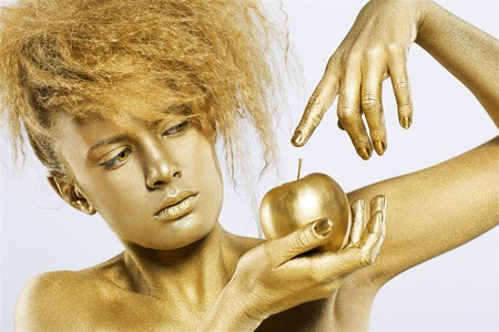 portrait of girl with golden bodyart posing with golden apple in her hands on grayの写真素材