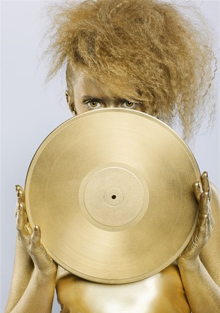 portrait of girl with golden bodyart holding golden vinyl disc in hands on grayの写真素材
