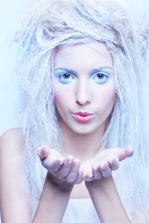 portrait of beautiful blonde frozen fairy girl blowing snow flakes from handsの写真素材