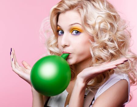 portrait of beautiful blonde party girl blowing up green balloonの写真素材