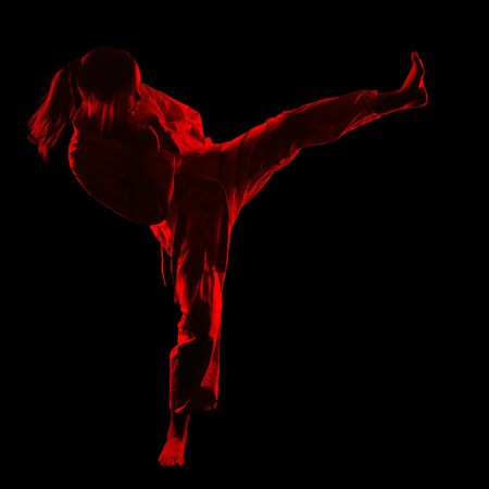 full-length silhouette portrait of beautiful martial arts girl in kimono excercising karate kata kick on blackの写真素材