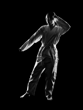 full-length silhouette portrait of beautiful martial arts girl in kimono excercising karate kata on blackの写真素材