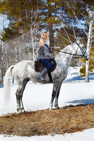 outdoor portrait of beautiful blonde girl in furs with pale horse in sunny winter forestの写真素材