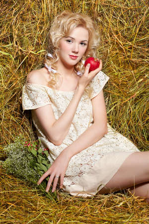portrait of beautiful blonde country girl sittitng on yellow hay with applesの写真素材