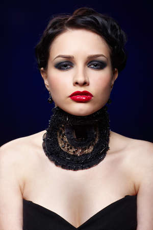 portrait of beautiful brunette girl posing on blue in black lacy collarの写真素材