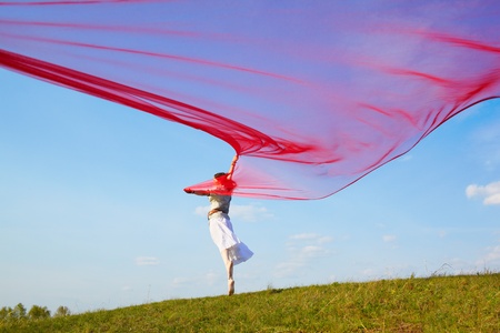 outdoor portrait of beautiful hippie girl running with big piece of red light cloth under the blue skyの写真素材