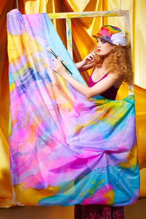 portrait of beautiful woman  artist with paintbrush standing behind the easel with painted cloth on itの写真素材