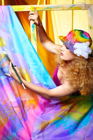 portrait of beautiful woman artist with paintbrush standing behind the easel with painted cloth on itの写真素材