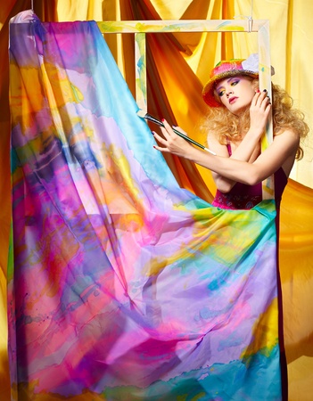 portrait of beautiful woman painter with paintbrush standing behind the easel with painted cloth on itの写真素材