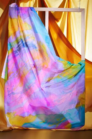 hanged wooden easel with painted colorful cloth on it. yellow silk cloth on backgroundの写真素材