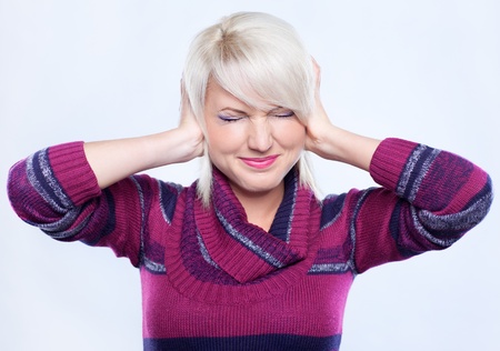 young woman in woolen sweater protecting ears from noiseの写真素材