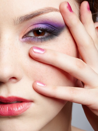 close-up half-face portrait of young beautiful woman with violet eye shadow touching her face with manicured handの写真素材