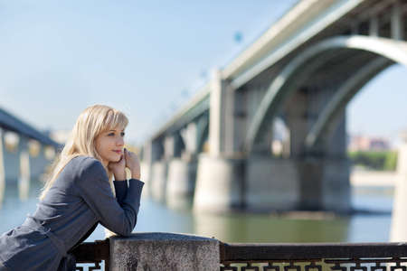 Beautiful woman leans on the railing of the bridge in the backgroundの写真素材