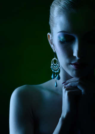 Blue tinted portrait of beautiful young blonde woman with hands below her chinの写真素材