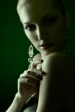 green toned portrait of beautiful young blonde woman in ear-rings touching her shoulder with manicured handの写真素材