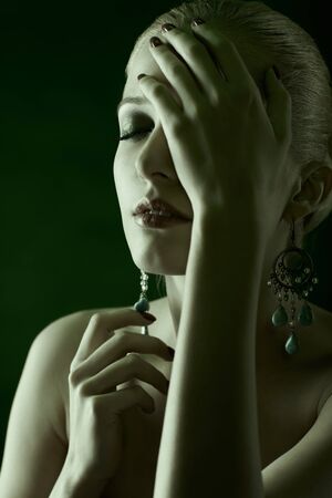 green toned portrait of beautiful young blonde woman in jewellery touching her faceの写真素材