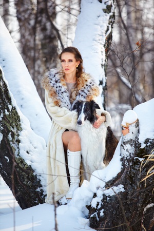 outdoor portrait of beautiful brunette woman with russian wolfhound in snowy winter forestの写真素材
