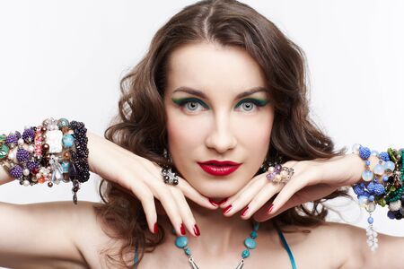 portrait of young beautiful brunette woman in blue dress and jewellery touching her face with manicured handsの写真素材