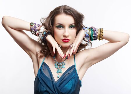 portrait of young beautiful brunette woman in blue dress and jewelry on grayの写真素材