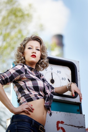 outdoor portrait of young beautiful blonde woman posing near gas pump with smoking stack on backgroundの写真素材