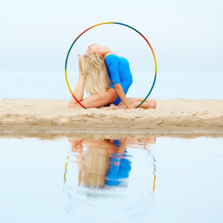 outdoor portrait of young beautiful blonde woman gymnast training with hula-hoop on the sandの写真素材