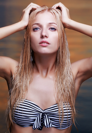 portrait of young beautiful blonde woman in bikini touching wet hair  sea waters on backgroundの写真素材