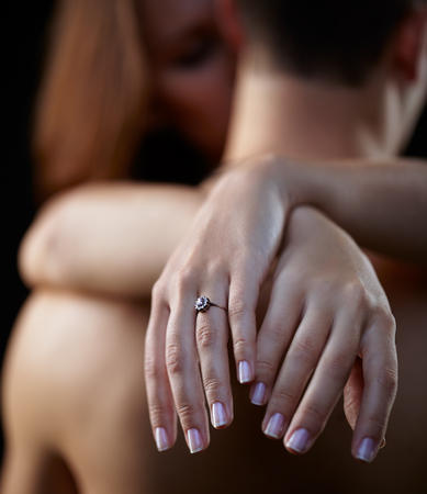 Young beautiful couple on black with female hands on foreground. Focus on ringの写真素材