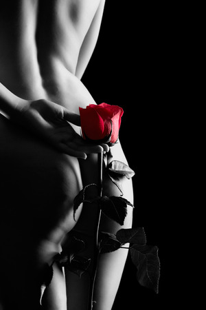 Silhouette of nude beautiful young woman  from back side with red rose in hands isolated on blackの写真素材
