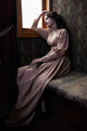 Young woman in beige vintage dress of early 20th century sleaping near window in coupe of retro railway trainの写真素材